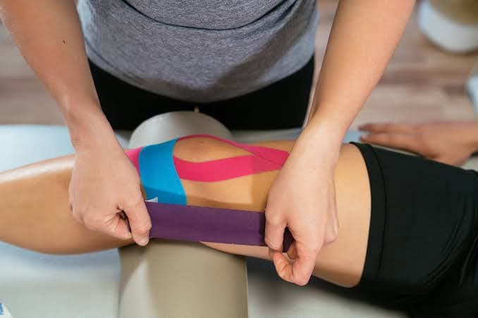 Physiotherapist applying kinesiology tape around a knee